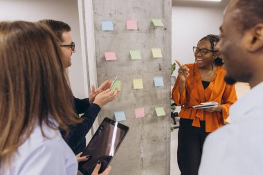 Professional team collaborating, writing strategy notes on colorful sticky papers during dynamic workplace brainstorming session clipart