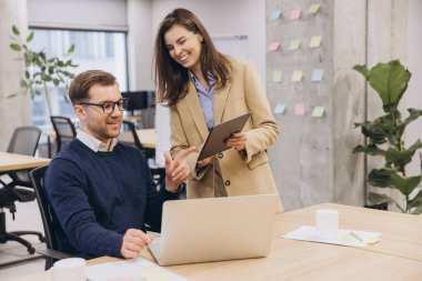 Çağdaş bir ofis ortamında iş birliği yapan iki profesyonel bilgisayar ve dijital tablet kullanarak verimli bir tartışmaya giriştiler.