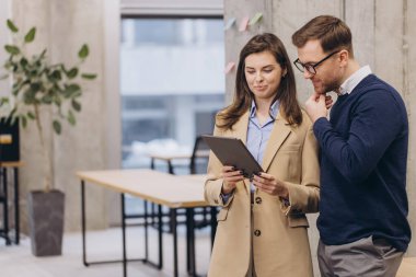 İki profesyonel iş adamı ve kadın modern ofis ortamında bir tablet üzerinde proje üzerinde tartışıyorlar, iş yerinde takım çalışması ve teknolojiyi ön plana çıkarıyorlar.