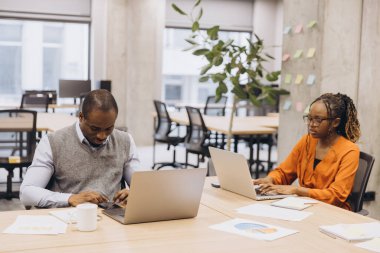 Modern ofis ortamında takım çalışması yapan Afro-Amerikan profesyoneller, dizüstü bilgisayar kullanıyor ve yaratıcı bir çalışma ortamında iş stratejilerini tartışıyorlar.