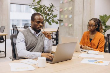 İki genç Afrikalı profesyonel, parlak, modern bir ofiste dizüstü bilgisayarlarına yoğunlaşıp bir proje üzerinde çalışıyorlar.