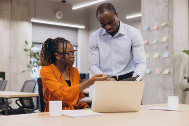İki Afrikalı Amerikalı profesyonel, çağdaş bir ofis ortamında, duvarında yapışkan notlar olan bir dizüstü bilgisayardan faydalanıyorlar.