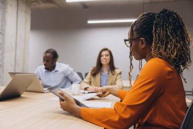 Profesyoneller, çağdaş bir ofis ortamında dijital cihazlardan yararlanarak, takım çalışması ve çeşitliliği vurgulayarak, işbirlikçi bir toplantıda yer aldılar.