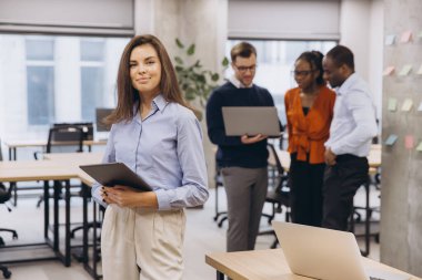 Kadın profesyonel kontrol tableti, çağdaş çalışma alanında dizüstü bilgisayarlar üzerinde işbirliği yapan çeşitli ekip, takım çalışmasını ve teknolojisini ön plana çıkarıyor