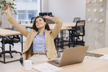 Profesyonel kadın ergonomik dizüstü bilgisayar ve minimalist tasarım ile gösterişli çalışma alanında otururken esniyor, dinleniyor.