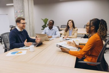Konferans masası etrafında işbirliği yapan profesyoneller çizelge ve fikirleri tartışıyor, modern ofis ortamında yenilik ve takım çalışmasını teşvik ediyorlar.