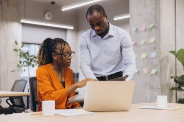 Çağdaş bir ofis içinde işbirlikçi bir projeye katılan çeşitli profesyoneller, iş ortamında takım çalışması ve yenilikleri vurguluyor