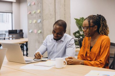 Çağdaş çalışma alanında işbirliği yapan Afrikalı Amerikalı profesyoneller, dizüstü bilgisayardaki proje detaylarını gözden geçiriyorlar, görüşlerini paylaşıyorlar.