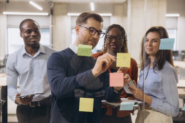 Çağdaş çalışma ortamında işbirliği yapan ekip toplantısı sırasında çeşitli profesyonellerin beyin fırtınası yapması, renkli notlarla fikirleri paylaşması