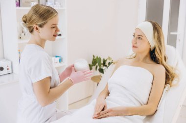 Güzellik uzmanı nemlendirici krem sürerken müşteri profesyonel cilt bakımı ile tedavi koltuğunda dinleniyor.