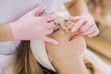 Kozmetik dermatoloji tedavisi sırasında hastanın burun kıvrımlarına botoks yapan eğitimli bir kozmetikçi.