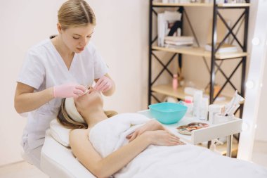 Profesyonel cilt bakımında yüz bakımı sırasında müşterinin yüzünü temizleyen pembe eldivenler giyen bir güzellik uzmanı.