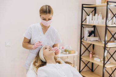 Kadın müşterinin alnına botoks yapan profesyonel güzellik uzmanı estetik kliniğinde kırışıklık azaltmayı hedefliyor.