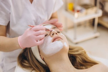 Steril eldiven giyen profesyonel güzellik uzmanı spa tedavisinde gençleştirici maske takıyor, cilt sağlığını ön plana çıkarıyor.