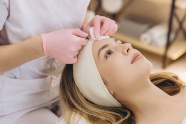 Klinikte kozmetik cilt bakımı sırasında kadın müşterinin alnına botoks yapan profesyonel güzellik uzmanı.