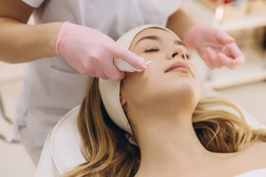 Güzellik uzmanının cilt bakımı sırasında cilt kremini yumuşatması, müşterinin profesyonel spa ortamındaki cildine odaklanması,