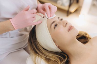 Yaşlanmayı önleyen yüz enjeksiyonunu gerçekleştiren yetenekli kozmetolog, profesyonel güzellik tedavisi sırasında alnındaki kırışıklıkları hedef alıyor.