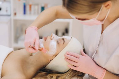 Cilt bakımı uzmanı spa ortamındaki bir müşteriye yüz maskesi takar, kozmetik uzmanlığı teknikleriyle rahatlama ve gençleşmeyi teşvik eder.