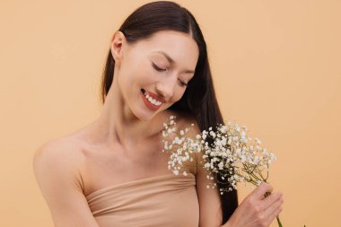 Güzel, gülümseyen esmer bir kadının stüdyo portresi. Elinde çigila çiçekleri ve bej arka planda saçıyla oynuyor.