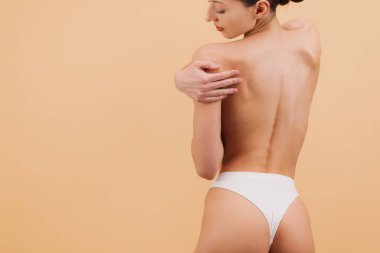 Omzunu kucaklayan bir kadın, zarif ve doğal güzelliğini yumuşak bir arka planda sergiliyor. Kişisel bakım ve vücut pozitifliğini vurgulamak