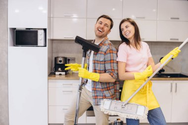 Ellerinde lastik eldiven olan gülümseyen çift mutfağı temizlerken eğleniyorlar.