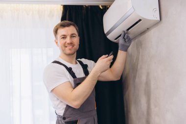 Gülümseyen tamirci bakım sırasında uzaktan kumanda kullanarak klima kuruyor.