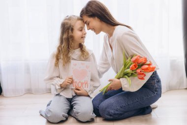 Annesine canlı laleler ve kalpten gelen bir tebrik kartı sunan kız. Anneler Günü 'nün mutluluğunu birlikte kutluyorlar.