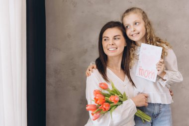 Gülümseyen annesine neşeli bir tebrik kartı ve canlı laleler sunan kız birlikte Anneler Günü 'nün neşesini kutluyorlar.