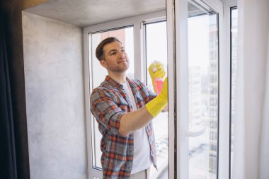 Sarı eldiven giyen hademe, pırıl pırıl temizliği sağlamak için sprey şişesi ve bez kullanıyor.