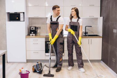Profesyonel temizlikçiler yerleri siliyor ve modern mutfağı, takım çalışmasını ve temizlik hizmetlerini süpürüyor.