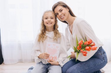 Gülümseyen kız Anneler Günü için annesine tebrik kartı ve kırmızı laleler veriyor.