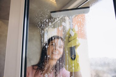 Lastik eldiven giyen temizlikçi, pencereyi deterjanla temizleyerek pırıl pırıl, pırıl ve lekesiz bir son garantiliyor.