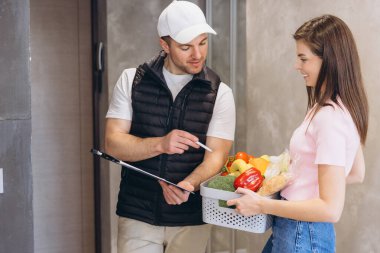 Teslimat notunu, içi taze yiyecek dolu sepeti tutan bir müşteriye sunan kurye market teslimatının kolaylığını vurguladı.