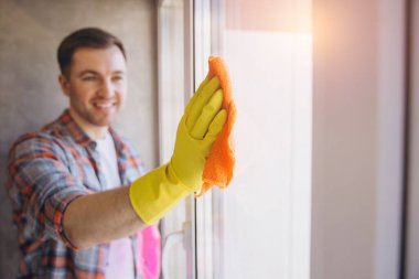 Eldiven ve bez kullanarak pencereyi temizleyen gülümseyen genç adam, temizlik hizmeti konsepti