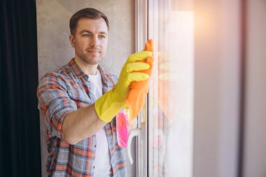 Temizlikçi pencereleri kumaş ve deterjanla özenle temizliyor. Parlak sarı eldivenler giyiyor. Pırıl pırıl ve pırıl bir son sağlıyor.