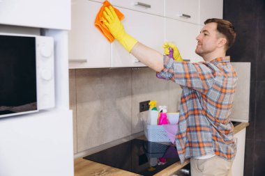 Eldiven giyen adam mutfak dolaplarını temizliyor temizlik ürünleri kullanıyor, modern apartmanda ev işleri yapıyor.
