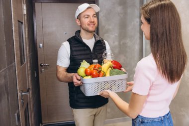 Kapısındaki müşteriye taze ürünlerle dolu bir sepeti teslim eden kurye.