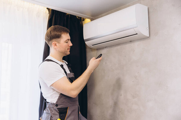 Technician is using a remote control to operate a modern wall mounted air conditioning unit, ensuring optimal cooling performance