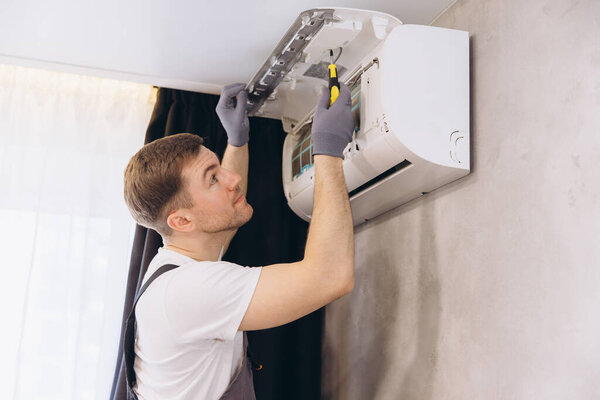 Plumber using screwdriver and wearing gloves repairing an air conditioning unit in a modern home