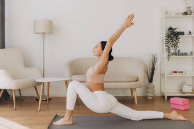 Oturma odasında yoga yapan genç bir kadın fiziksel aktivite yoluyla sağlığını ve sağlığını arttırıyor.