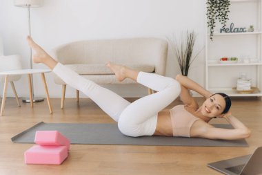 Bilgisayarındaki beden eğitimi dersinden sonra evdeki paspasın üzerinde bisiklet mekiği çeken sağlıklı bir kadın.