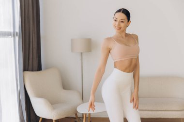 Oturma odasında yoga yapan sağlıklı bir kadın ev ortamında huzurlu bir anın tadını çıkarırken sağlığını ve sağlığını kucaklıyor.