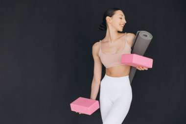 Elinde yoga ekipmanları olan mutlu bir kadın şık bir kapalı mekan stüdyosunda canlandırıcı bir egzersiz rutinine hazırlanıyor.