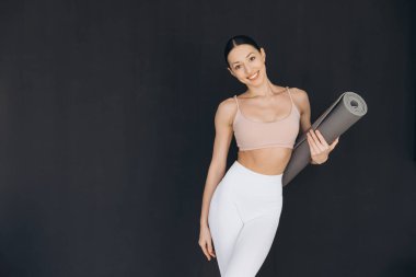 Yoga hocası, siyah arkaplan üzerine yoga kursuna başlamadan önce gülümsüyor ve yoga minderi tutuyor.