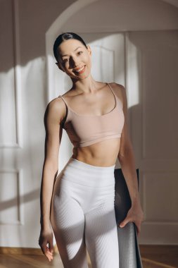 Elinde yoga minderi tutan sağlıklı ve dengeli bir yaşam tarzını evdeki düzenli egzersizlerle destekleyen sağlıklı bir kadın.