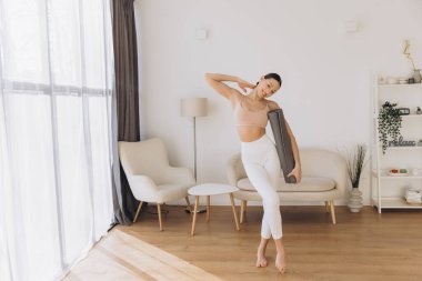 Elinde yoga minderi tutan sağlıklı bir kadın, rahat dairesinde canlandırıcı bir antrenmana hazırlanıyor, sağlıklı ve aktif bir yaşam tarzını kucaklıyor.