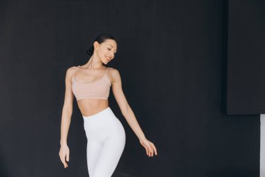 Siyah bir duvarın karşısında yoga yapan genç bir kadın rahat bir ev ortamında huzurlu bir atmosfer yaratıyor.