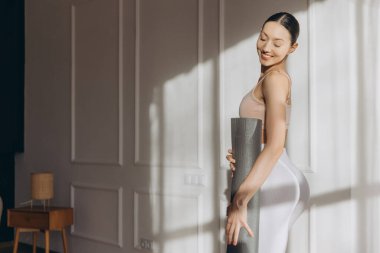 Yoga minderi tutan mutlu bir kadın, evde sağlıklı yaşam tarzının ve sağlığının tadını çıkarıyor.