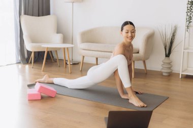 Konforlu bir oturma odasında dizüstü bilgisayarla yoga yapıyor, çevrimiçi derslere giriyor ve sağlığını arttırıyor.