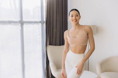 Spor kıyafetleri giyen sağlıklı bir kadın evinde yoga yapıyor, gülümsüyor ve dinleniyor.
